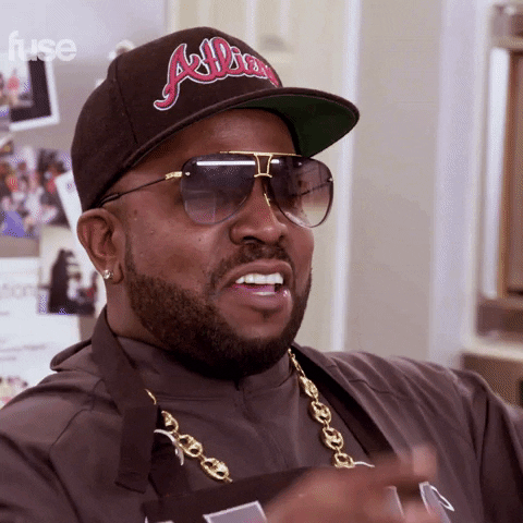 Celebrity gif. Rapper Big Boi on Made from Scratch smiles and raises his hands in the air in praise. Text, “lawd.”