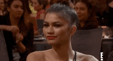 Celebrity gif. Closeup of Zendaya giving us the side eye before she forces a taut smile.