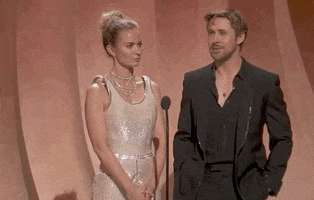 Oscars 2024 gif. Incredulously, Emily Blunt tosses her head and shrugs in confusion while saying, "Wow. Bit of a frosty hello." With his hands stuffed in his pockets, Ryan Gosling slowly scans the crowd with squinted eyes. 