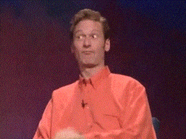 Reality TV gif. Ryan Stiles on Whose Line Is It Anyway sits on stage and makes his fingers into a circle and thrusts a finger through the circle towards Drew Carey. Drew looks back at him smiling and then makes a blowjob gesture with a thrusting fist and his tongue on his cheek.