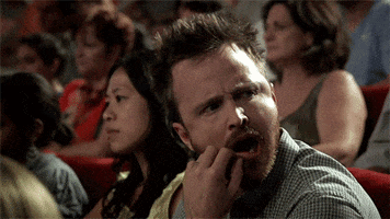 Late Night gif. Aaron Paul sits in a theater with others, looking peeved while frowning, shaking his head, and scratching his mouth before shouting "booooo, bitch."