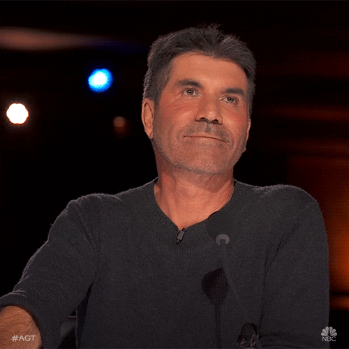 TV gif. Simon Cowell in America's Got Talent gives us a wink and a smile.