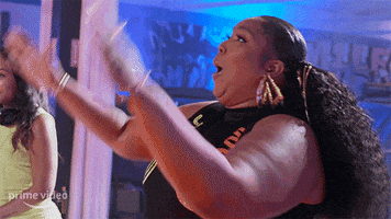 Reality TV gif. From Watch Out for the Big Grrrls, Lizzo wears a sleeveless dress with her hair pulled back, clapping her hands proudly.