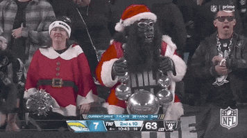 Video gif. Oakland Raiders fan dressed in a gorilla costume with sunglasses and a Santa hat and jacket, holding an oversized necklace that consists of silver balls that look like giant bling. 