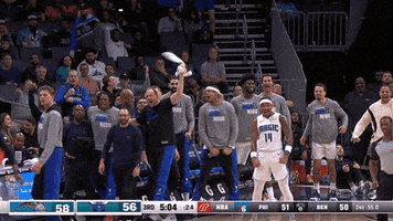 Sports gif. Orlando Magic basketball player #14 Gary Harris making an excited gesture of strength with his arms while turning to his team on the sidelines who are also celebrating gaining a two point lead.