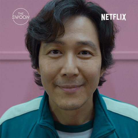 TV gif. Lee Jung Jae as Gi Hun in Squid Game. He's taking a picture for his ID photo and he gives us a blank, derpy, wide grin showing his naviete.