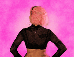 Celebrity gif. Doja Cat, back to us, turns to look over her shoulder, and smiles saying "hey."
