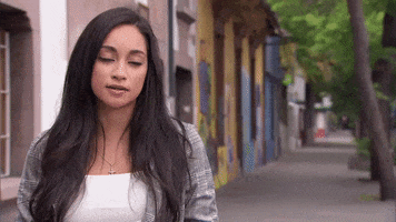 Reality TV gif. Victoria Fuller on The Bachelor shrugs with an uncertain half smile as she stands on a tree-lined sidewalk.