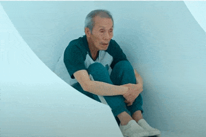Photo gif. O Yeong-su as Oh Il-nam in Squid Game. He is sitting in the corner of a room with his legs drawn up to his chest and he's hugging his legs, looking sad. Text, "Waiting for you."