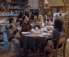 Friends gif. All of the friends, gathered around a holiday table, raise their glasses and cheers together.