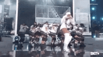 Celebrity gif. Mary J. Blige at the 2019 BET Awards, performing in white with a group of dancers behind her, as they all hop forward in unison.