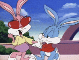 Cartoon gif. Buster Bunny kneels as he holds a hand of a giddy Babs Bunny. Her pink ears form a heart as she bashfully blinks red hearts from her eyes. 