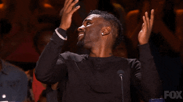 Reality TV gif. In a clip from SYTYCD, a grinning Jason Derulo claps his hands together in gratitude and he speaks over his shoulders to the applauding audience.