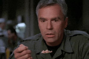 TV gif. Richard Dean Anderson as Jack O'Neill in Stargate SG-1 drops a spoonful of food and cradles his head in his hand.