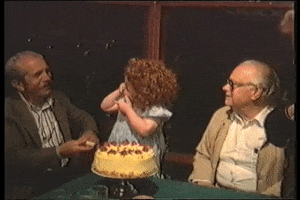 Video gif. A young girl stands in front of a birthday cake and stares at the man next to her. She then loses her balance and her head slams into the cake and she falls onto the ground. She cries and has icing all over her mouth and chin. 