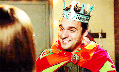 TV gif. Jake Johnson as Nick in New Girl wears a cape and a paper crown as he shakes his head and smiles weakly, then looks like he's going to be sick.