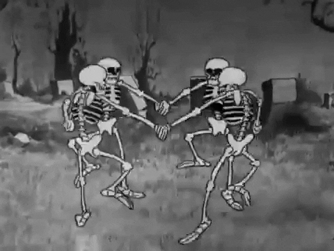 Cartoon gif. Four skeletons hold hands and excitedly dance in a circle in a desolate cemetery with barren trees and gravestones.