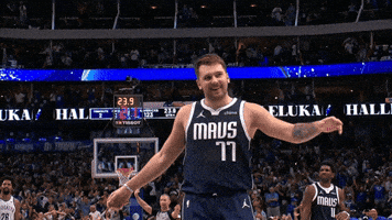Sports gif. Luka Doncic of the Dallas Mavericks is on the court and whoops while he raises a hand and spins it in celebration.