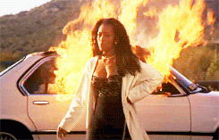 Movie gif. Angela Bassett as Bernadine in Waiting to Exhale is dressed in a lacy black shift dress and a white robe as she walks away from a car she set on fire. She looks angry but satisfied and points ahead with one arm as she walks away.