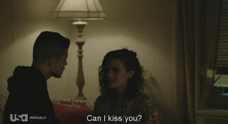 TV gif. Rami Malek as Elliot Anderson and Frankie Shaw as Shayla Nico in a dim bedroom share a passionate kiss after Malek asks “Can I kiss you?”