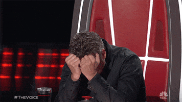 Reality TV gif. Blake Shelton sitting with his elbows on the table and his head in his hands, stewing.