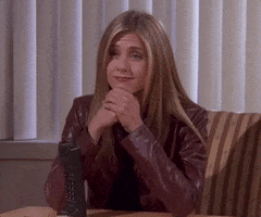 Friends gif. Jennifer Aniston as Rachel sits with her elbows on a desk, resting her chin on her hands as she waves with both of her hands, smiles, and says, "Hi."