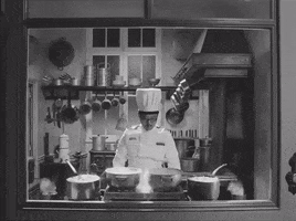 Movie gif. Stephen Park as Chef Nescaffier in The French Dispatch quickly sharpens a knife while standing in front of a stove with four full pots and billowing flames on either side.