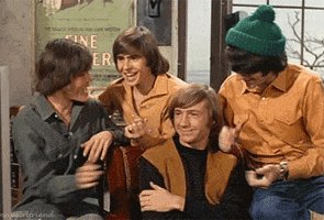 TV gif. Members of the Monkees clap and cheer excitedly, patting Peter Tork on the shoulder, who smiles, proud.