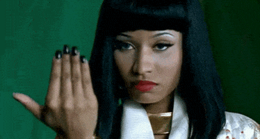 Celebrity gif. Nicki Minaj glares menacingly ahead. She closes the fingers of her outstretched hand as if signaling, bring it on.
