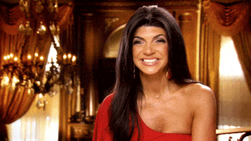Reality TV gif. Teresa Giudice from Real Housewives of New Jersey. She waves eagerly while being interviewed and grins.