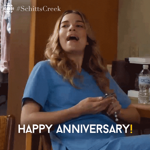 Schitt's Creek gif. Annie Murphy as Alexis leaned back in her chair, looking up from her phone to smile and say, "Happy anniversary!" 