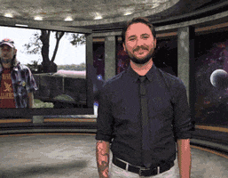 TV gif. Wil Wheaton on the Wil Wheaton Project stands in a CGI space deck with windows that look out to the galaxy. A large screen behind him has a random man on it. WIl Wheaton looks at us, nodding and clapping. 