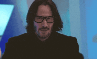 Movie gif. Keanu Reeves in Always Be My Maybe walks towards up, tilting his head, and holding his hands up to shrug like nothing bothers him.