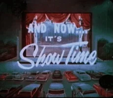 Un écran de cinéma en plein-air face à des voitures garées (drive-in) et est écrit "and now, it's show time"