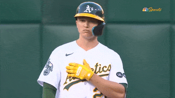 Sports gif. Zack Gelof in a batter's helmet of the Oakland Athletics swipes his arm straight across his chest doing a baseball sign as he nods his head with a frown like, "This is the move."