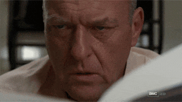 TV gif. Dean Norris as Hank in Breaking Bad looks up from a paper he's reading and realization hits his face. He looks shocked and livid, as he's just figured out something life changing.