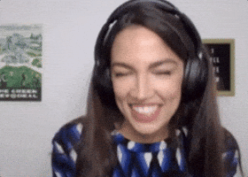 Political gif. Alexandria Ocasio-Cortez fans her face and throws her head back indicating heat before coming back towards the screen, smiling.