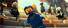 Cartoon gif. Benny from the Lego Movie is slowly floating up and he smiles and waves jovially while saying, "Hello!" without concern.