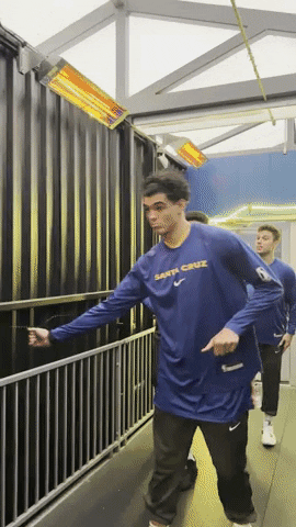 Sports gif. Basketball player Guilherme Santos does a figure 8 dance move with his hips as he walks forward and other players walk behind him in a simple line. 
