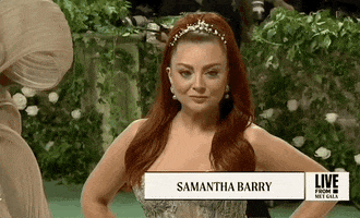 Met Gala 2024 gif. Tilt down through Samantha Berry smiling for the cameras, closeup on her antique gold Atelier gown with a structured peplum bodice and tulle skirt, and out.