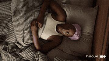 TV gif. Camera rotates and closes in on Issa Rae on Insecure as she lays in bed with a blank expression, thinking.