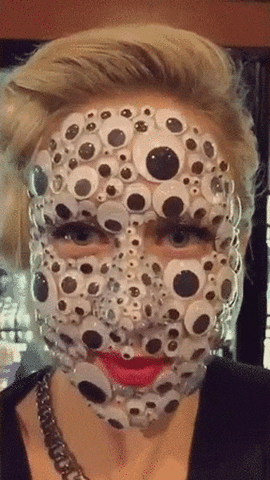 Video gif. A woman gently shakes her head. Except for her eyes and lips, her face is completely covered in different sizes of googly eyes.