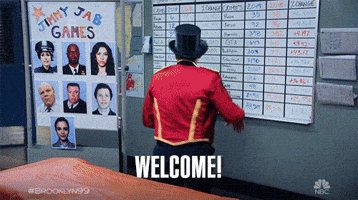 TV gif. Jo Lo Truglio as Charles in Brooklyn Nine Nine spins around to face the camera wearing a marching band conductor's jacket and a top hat. He spreads his arms wide, as if to say, "ta-daaa!" Text, "Welcome!"