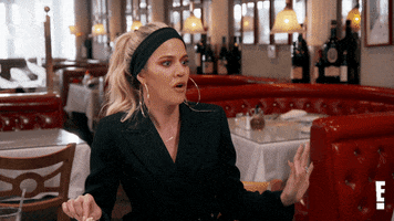 Reality TV gif. Khloe Kardashian sits in a mostly empty restaurant, surprised and uncomfortable with what she's just heard. She makes quick gestures between herself and someone offscreen, then holds up a palm to shut down the topic.