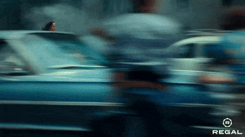 Movie gif. Gal Gadot as Wonder Woman dashes along the street past cars and people.