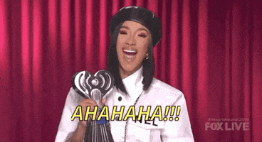 Celebrity gif. Cardi B holds an iHeartRadio award and leans back, cackling.
