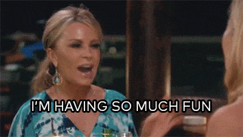 Reality TV gif. Tamra Judge on The Real HouseWives of Orange County sits across from another woman at a restaurant. Tamra leans over, shaking her hand, and says, “I'm having so much fun!”