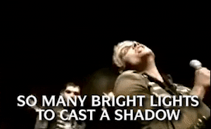 Music video gif. Gerard Way in the video My Chemical Romance for Famous Last Words looks down at us as he sings menacingly. Text, "So many bright lights to cast a shadow."