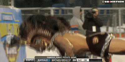 Sports gif. A man wearing traditional Aztec ceremonial headpiece and gear is doing pushups at the Famous Idaho Potato Bowl.