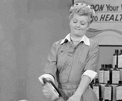 TV gif. Lucille Ball in I Love Lucy stands at a countertop with a display of cough syrups behind her, tipping a bottle to her lips and guzzling its contents.